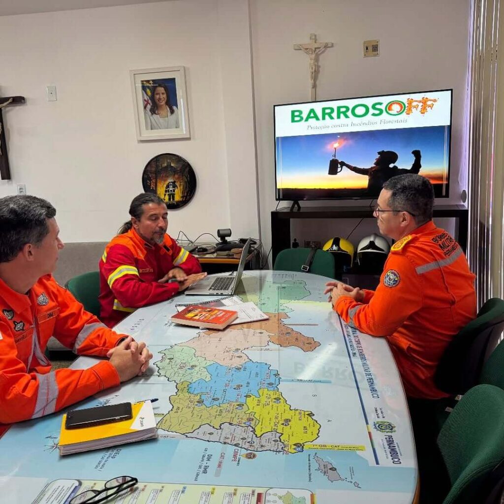 eunião institucional da Barrosoff Engenharia com oficiais do Corpo de Bombeiros Militar de Pernambuco (CBMPE) em volta de uma mesa com mapa do estado e tela exibindo a marca Barrosoff.